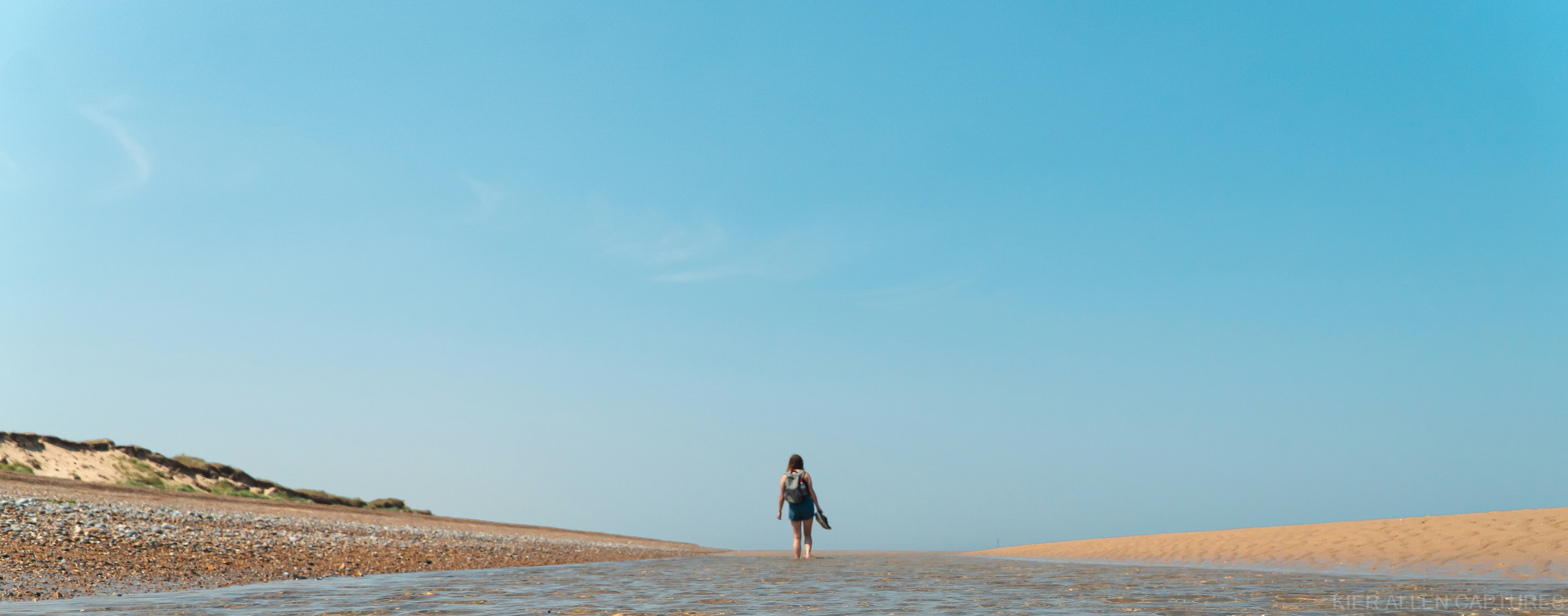 woman in black dress walking on brown sand during daytime